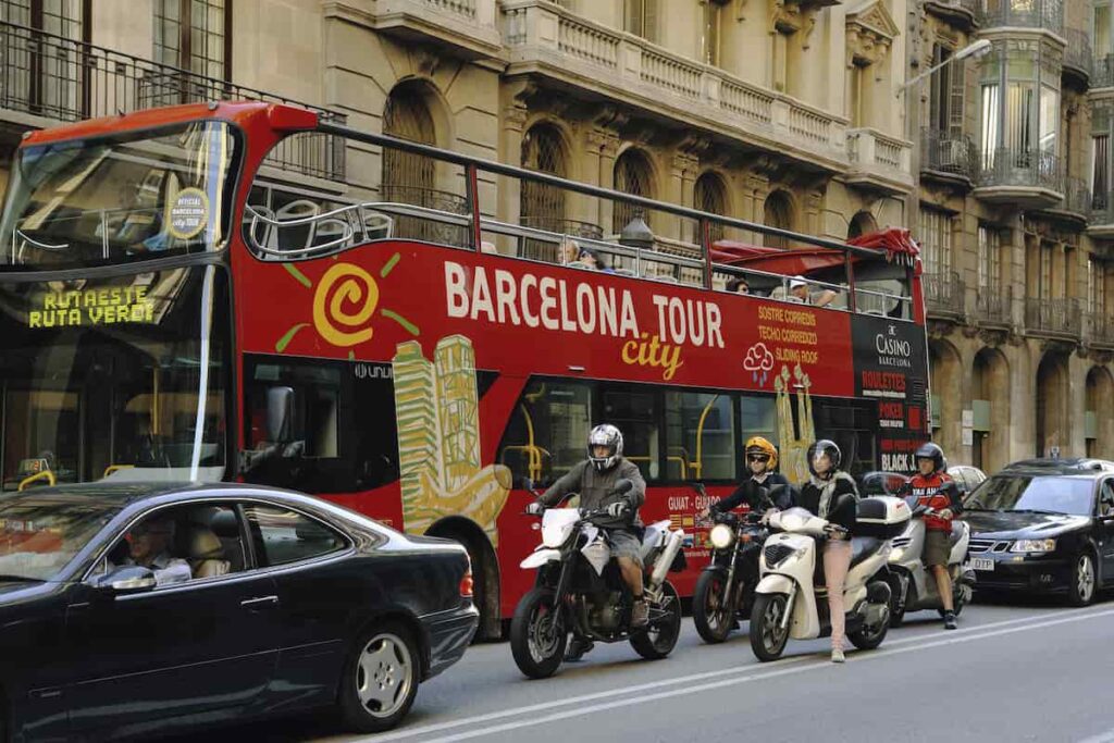 Big red bus with Barcelona city tour service on the Via Laietana street between cars and motorbikes and will ask yourself is Barcelona safe?