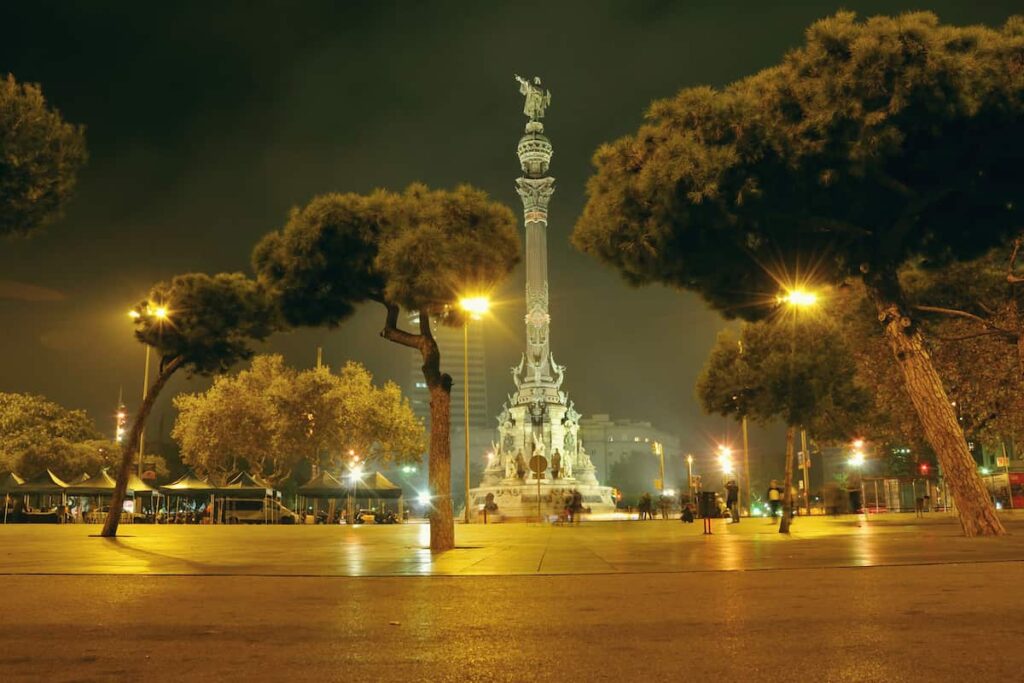 Park trees in the area close to the port of Barcelona with statue of Christopher Columbus on backward is one of the best places to visit in Barcelona at night.