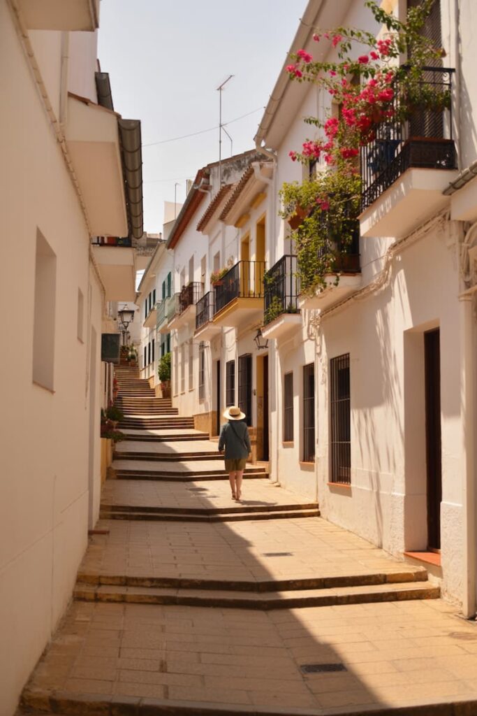 Person in a hat walking up a sunlit stepped street lined with flowers in one of the best towns to visit on the Costa del Sol